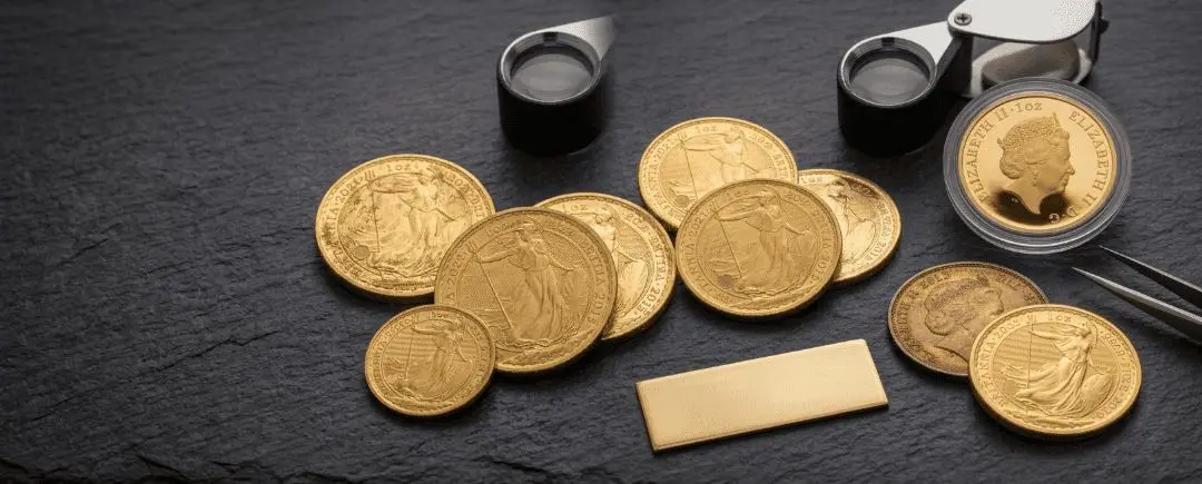 Gold Britannia coins on slate with a loupe, tweezers and a gold bar