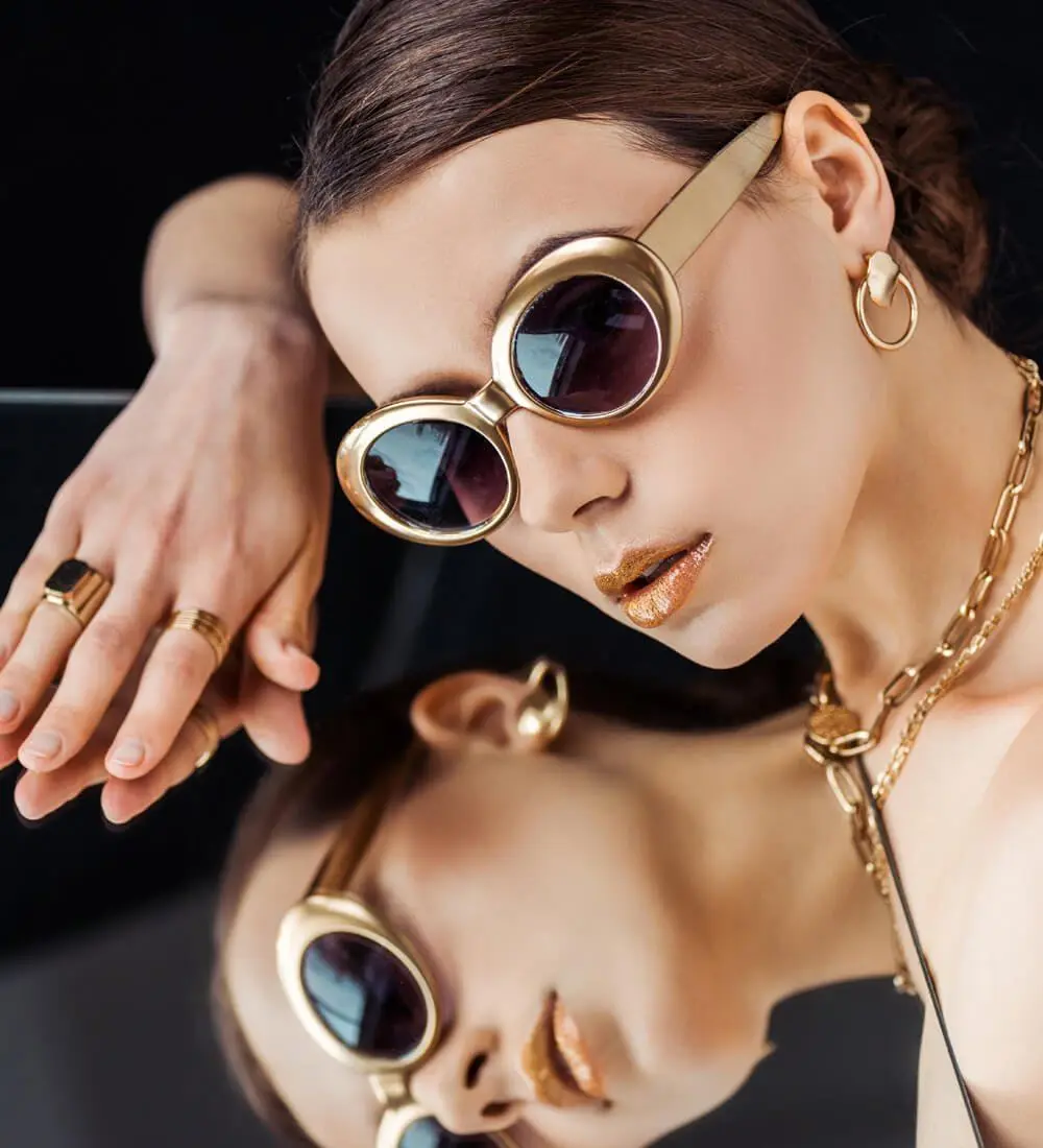 Model wearing gold sunglasses, gold hoop earrings, rings and layered chains