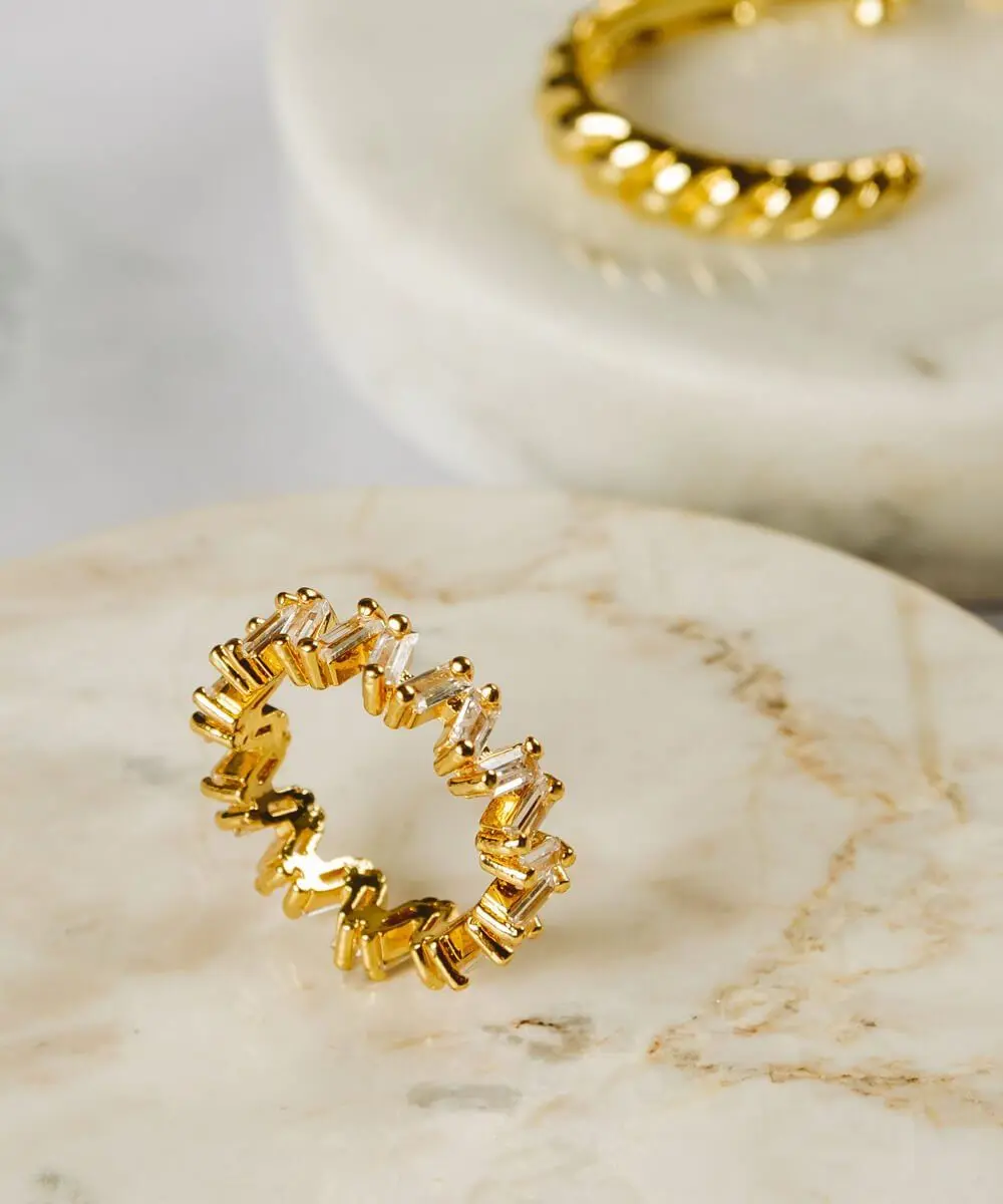 Gold eternity ring with baguette stones on a marble dish