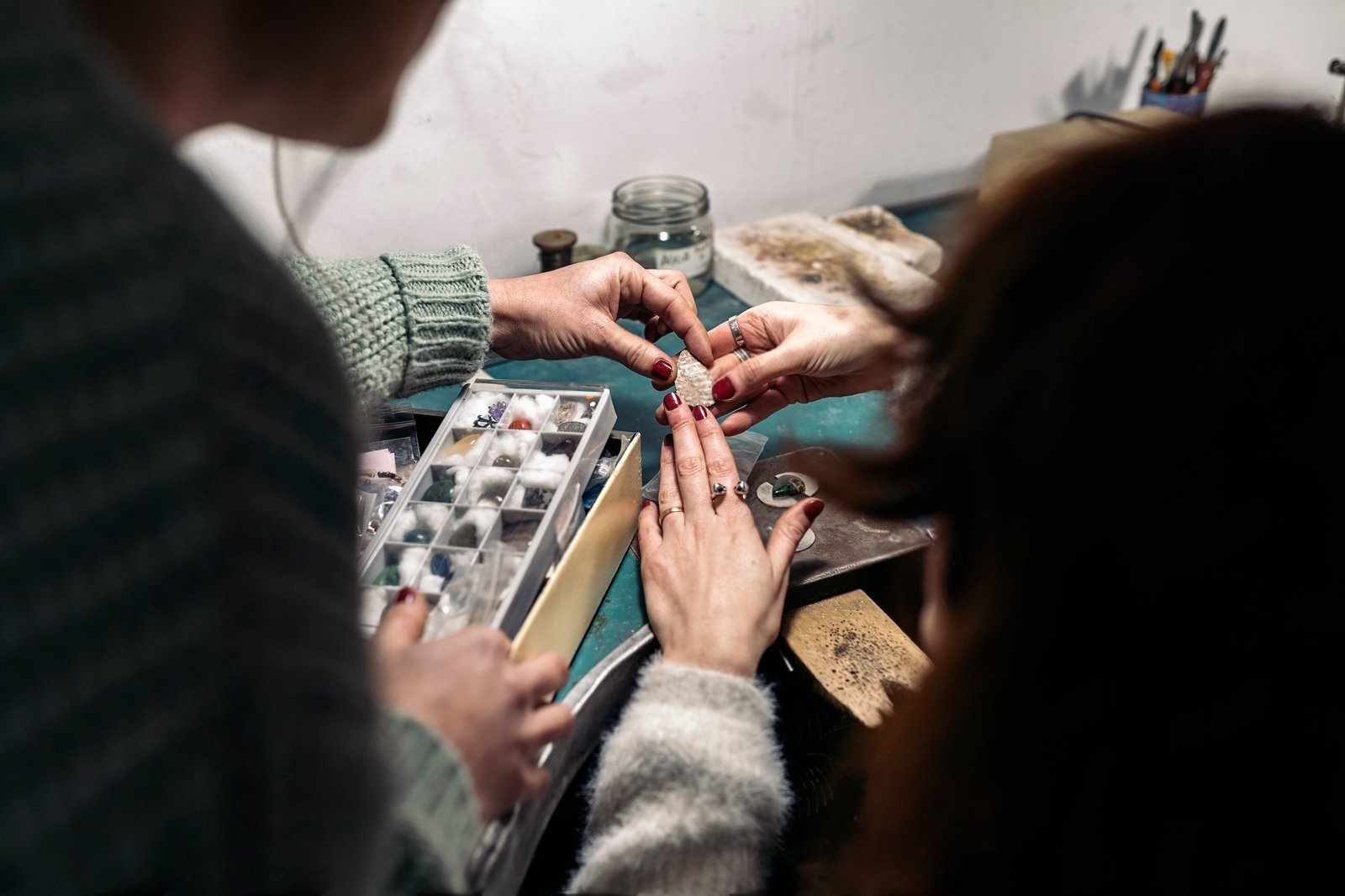 Two individuals carefully examine a loose gemstone over a jeweler's workbench alongside an organizer of assorted stones, representing the personalized, hands-on process of creating Custom Engagement Rings Little Rock for those seeking unique Bespoke Engagement Rings and unforgettable Engagement Rings.
