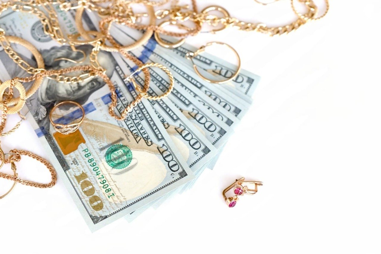 A close-up view of various gold chains, rings, and earrings resting on a fan of US hundred-dollar bills, illustrating the lucrative opportunity of finding the best Scrap Gold Near Me to get top Cash for Scrap Gold Near Me.