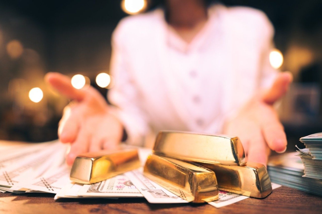 A professional gesturing toward gleaming gold bars resting on a pile of hundred-dollar bills, illustrating the highly lucrative opportunity to Sell Gold Little Rock AR when visiting a premier Gold Bullion Dealer Little Rock or trusted Gold and Silver Buyer Little Rock.