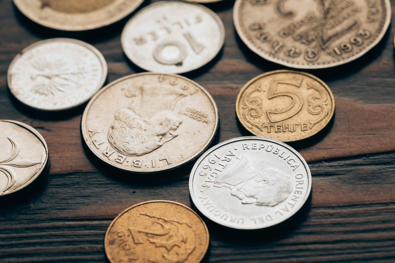 A close-up of various old and international coins scattered on a dark wooden table, representing the valuable collections you can bring in to secure the Best Rates for Selling Coins from a trusted Coin Dealer Little Rock or a premium Pawn Shop North Little Rock AR.