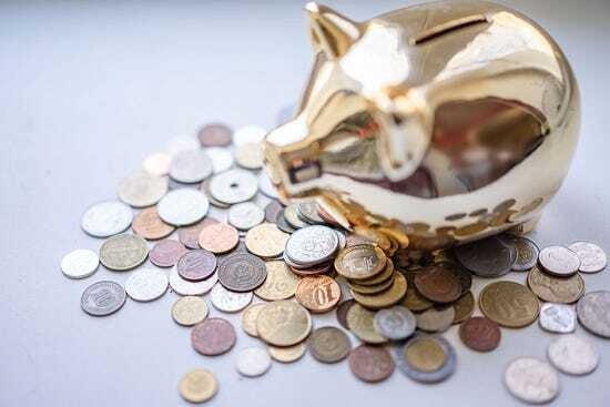 A shiny gold piggy bank sitting on a clean surface next to a scattered pile of silver and bronze coins, beautifully illustrating how to maximize your cash for gold little rock returns by choosing a trusted local precious metals buyer.